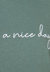Grønt stof med hvid kursiv tekst, der lyder "en dejlig dag" trykt henover.