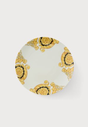Plato redondo de cerámica blanca con elaborados patrones florales en amarillo y negro que decoran los bordes sobre un fondo liso.