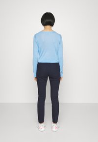 Suéter de manga larga azul claro combinado con pantalones ajustados azul marino y zapatillas blancas con detalles rojos. Fondo liso.