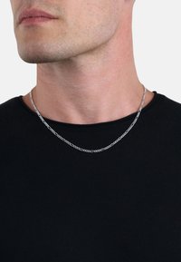 Collar de cadena de plata con eslabones ovalados, usado sobre una camisa negra. Los eslabones están pulidos con una textura suave.