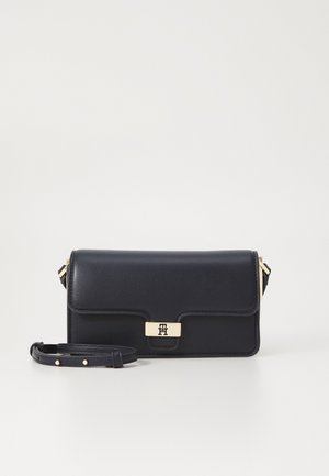 Czarna skórzana torebka na ramię z klapką i prostokątną złotą klamrą, regulowany pasek z złotymi ćwiekami, na białym tle.