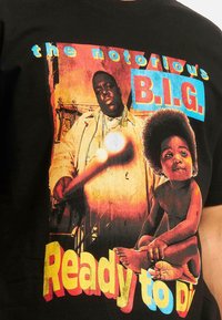 T-shirt en coton noir avec impression graphique vive d'un homme et d'un enfant, avec le texte en gras "the notorious B.I.G." et "Ready to Die" en jaune et bleu.