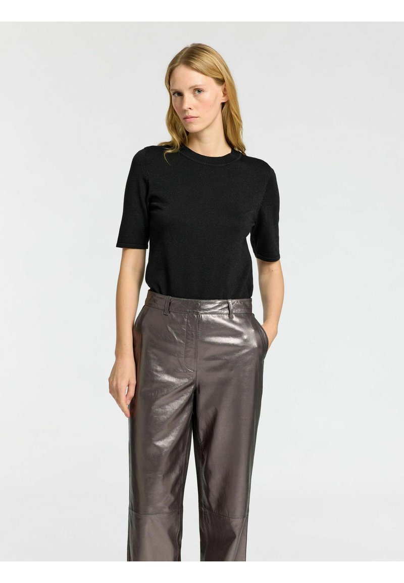 Musta lyhythihainen neulepaita, jossa on pyöreä pääntie, yhdistettynä kiiltäviin, metallinhohtoisiin ruskeisiin korkeavyötäröisiin housuihin, jotka korostavat rentoa istuvuutta.