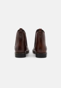 Bottes Chelsea en cuir marron avec une finition lisse, bout rond, panneaux latéraux élastiques et languettes en cuir au talon. Semelle en caoutchouc noire.