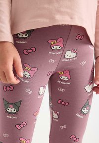 Barn i lila leggings med upprepade tryck av Hello Kitty, My Melody och Kuromi-karaktärer, samt en ljusrosa långärmad tröja.