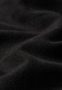 Detailní záběr černé pletené látky s viditelnou texturou a jemnými záhyby vytvářejícími jemné stíny.