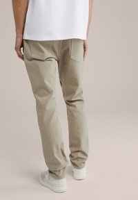 Beige katoenen broeken met een slim fit, voorzien van achterzakken en gecombineerd met witte sneakers. De stof heeft een gladde textuur.