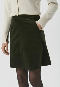 Groene corduroy rok met een A-lijn vorm en zijzakken, gecombineerd met een licht beige gebreide trui. Zachte textuur en gestructureerd ontwerp.