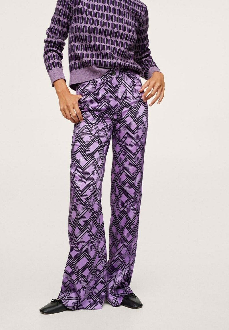 Pantalons violets à motifs avec des designs en zigzag noir. Fabriqués en tissu lisse, avec une coupe décontractée et des jambes évasées, associés à un pull violet à motifs.