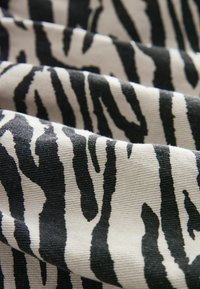Bomuldsstof med markante sort-hvide zebra striber, med en struktureret overflade og let ribbing, der viser skiftende mønstre.