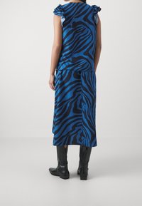 Sinivalkoraidallinen hihaton paita röyhelöillä olkapäillä, yhdistettynä vastaavaan hameeseen ja polven korkeisiin mustiin saappaisiin.