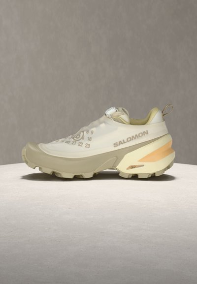 Μπεζ παπούτσι για τρέξιμο σε μονοπάτια Salomon με παχιά ανθεκτική σόλα, κυκλικό σχέδιο αρίθμησης στο επάνω μέρος και θηλιά στο τακούνι.