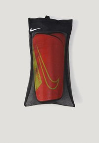 Parastinchi Nike Mercurial in una borsa di stoccaggio in rete nera. Presentano un design audace rosso con accenti verdi, con il logo e il marchio Nike.