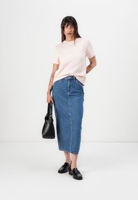 Lys rosa t-skjorte med korte ermer, blå denim maxiskjørt, svarte loafers, holder en svart håndveske. Minimalistisk design, avslappet passform.