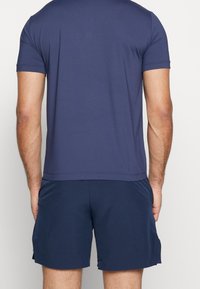 Námořnické sportovní tričko s krátkými rukávy, hladkým povrchem a rovnou spodní hranou, doplněné o odpovídající šortky s síťovanými bočními panely.