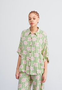 Patroon groene blouse met rozenmotief in het roze, knopen aan de voorkant, korte mouwen en een relaxte pasvorm. Vergezeld van bijpassende patroonbroeken.