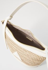 Sac à main tissé beige avec une garniture en cuir blanc, une fermeture éclair dorée et une poignée supérieure. L'intérieur dispose d'une doublure lisse et d'une poche zippée.