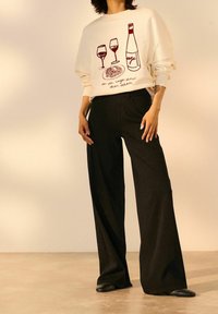 Sudadera crema con gráfico de copas de vino y botella; pantalones anchos negros; textura suave; corte relajado; diseño minimalista.