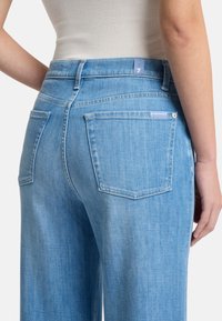Hellblaue Jeans mit lockerer Passform, Fünf-Taschen-Design und Nähten als Akzent. Der Bund hat hinten ein Etikett.