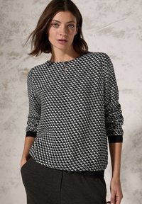 Schwarzer und weißer Pullover mit geometrischem Muster, rundem Ausschnitt, langen Ärmeln und gerippten Bündchen. Minimalistisches Design mit subtilen Details.