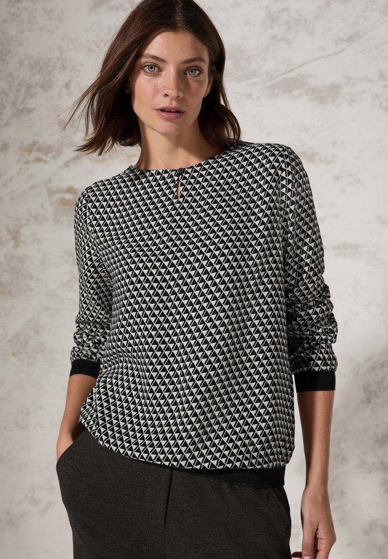 Schwarzer und weißer Pullover mit geometrischem Muster, rundem Ausschnitt, langen Ärmeln und gerippten Bündchen. Minimalistisches Design mit subtilen Details.