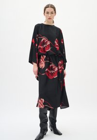 Rochie neagră, cu imprimeu floral, cu mâneci lungi și croială lejeră, având flori roșii și roz, asortată cu cizme negre până la genunchi.