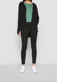 Svart zip-up hoodie, grön t-shirt och svarta rutiga leggings. Vita sneakers. Mjukt tyg, figurnära design och rutigt mönster på leggings.