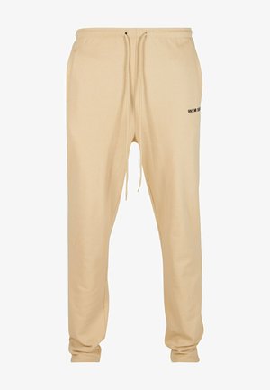 Bež pamukove trenirke s elastičnim pojasom, podesivom užešcu, bočnim džepovima i suptilnim crnim natpisom na lijevoj nozi.