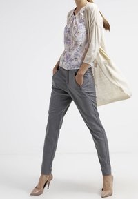 Ljust grå skräddarsydda byxor med sidofickor, kombinerade med en blus i blommönster i mjuka pastellfärger och en krämfärgad kofta.