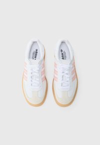 Chaussures de sport blanches avec des rayures rose clair. Présentent des accents en daim et une semelle en caoutchouc gomme. Lacets et semelles intérieures de marque visibles. Design classique.