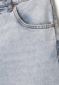 Jeans de denim azul claro con un bolsillo frontal, costuras visibles y una textura suave con patrones de desvanecimiento sutiles.