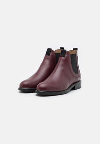Botas Chelsea de piel burdeos con paneles laterales elásticos, punta redonda, suela plana y un detalle de costura mínimo, que ofrecen un diseño elegante.