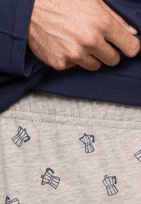 Navy long-sleeve shirt paired with light gray pants featuring a repeated print of coffee makers in dark blue. Fabrics appear soft and breathable.
