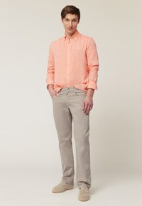 Chemise boutonnée en lin orange clair, chinos gris clair, mocassins beiges. Design simple avec une coupe décontractée. Pas de motifs ou d'accents visibles.