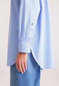 Camicia button-up a righe blu e bianche con maniche lunghe, caratterizzata da una vestibilità su misura, strisce a contrasto sui polsini e un dettaglio del logo sul polsino.