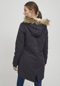 Mörk marinblå parkas med fuskpäls på huven, dragsko i midjan och bakventil; tillverkad av ett slitstarkt tyg med en jämn yta.