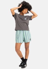 Gray cropped t-shirt with a small logo, paired with green and blue striped shorts. Worn with black sneakers and crew-length socks.