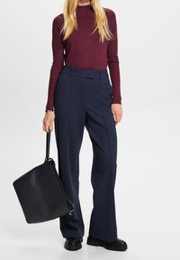 Bordowa bluzka z długim rękawem w połączeniu z granatowymi, szerokimi spodniami z wysokim stanem. Czarna torba o płaskim kształcie. Gładka tkanina i uporządkowana sylwetka.