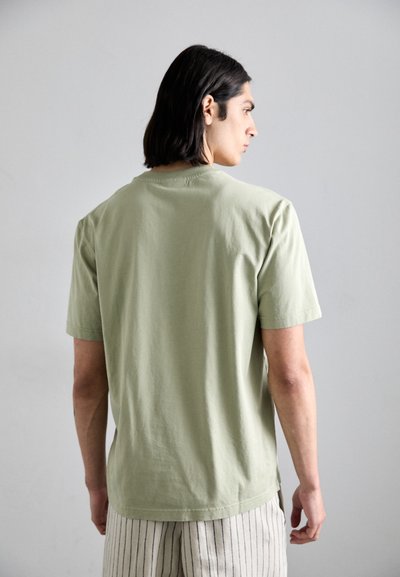 Tricou din bumbac verde deschis, cu mâneci scurte, guler rotund și o croială lejeră. Textură netedă, design minimal, fără logo-uri sau grafică vizibilă.