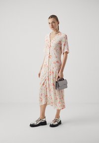 Rochie midi florală cu mâneci scurte și decolteu în V; modele multicolore pe un fundal deschis. O pereche de pantofi argintii strălucitori și o geantă gri.