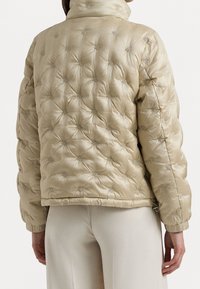 Beżowa pikowana kurtka puchowa z wysokim kołnierzem, prezentująca miękkie, błyszczące wykończenie, subtelne nadruki z logo RFE oraz elastyczne mankiety zapewniające dopasowanie.