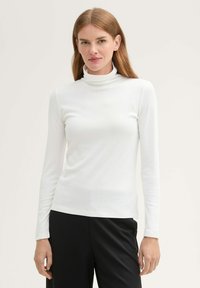 Weißes Langarm-Turtleneck-Oberteil mit taillierter Passform und weicher Textur, kombiniert mit schwarzen Hosen.