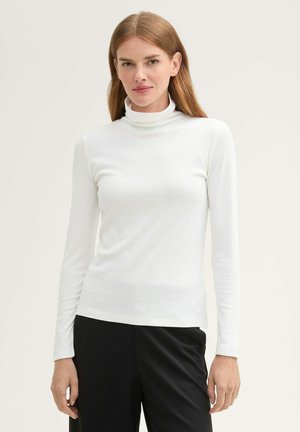 Weißes Langarm-Turtleneck-Oberteil mit taillierter Passform und weicher Textur, kombiniert mit schwarzen Hosen.