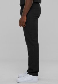 Pantalons noirs ajustés, fabriqués en mélange de coton. Présentent des poches latérales et sont portés avec des baskets blanches. Design épuré, détails minimaux.