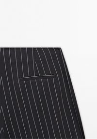 Pantalons à rayures noires avec un design épuré, dotés d'une poche arrière unique à ouverture étroite. Le matériau semble texturé.