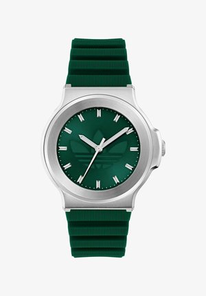 Montre verte avec un bracelet en silicone texturé. Un boîtier rond en argent entoure un cadran vert foncé avec des index blancs et un logo stylisé.