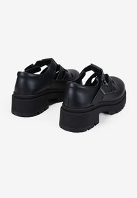 Zapatos de plataforma de cuero negro con diseños recortados y correa ajustable. Presentan suelas gruesas y texturizadas para mayor agarre y estabilidad.