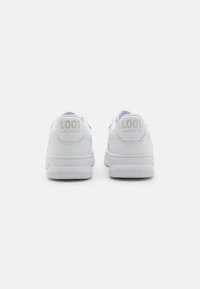 Par av vita Lacoste L001-sneakers visade från baksidan, med texturerat läder och präglad branding på hälfliken.