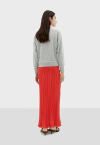 Sweatshirt gris avec des poignets et un ourlet côtelés, associé à une jupe maxi plissée rouge, porté avec des sandales noires à lanières.