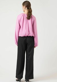 Fuchsia lyserød bluse med løs pasform og indsamlet halsudskæring, kombineret med sorte bukser med vide ben. Glat stof med lange ærmer.